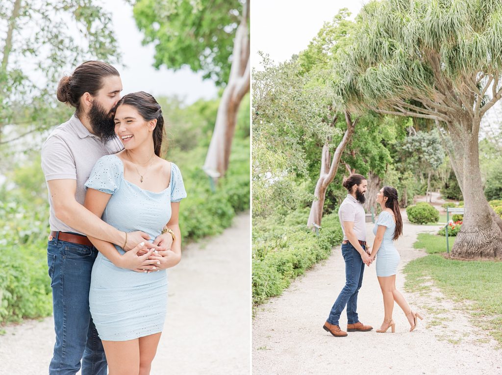 Engaged couple laughing on a white dirt path surrounded by trees. 