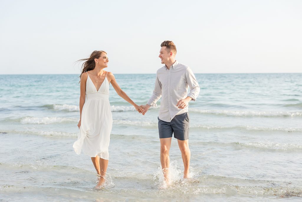 A couple running through the water during their engagement session on the beach. 