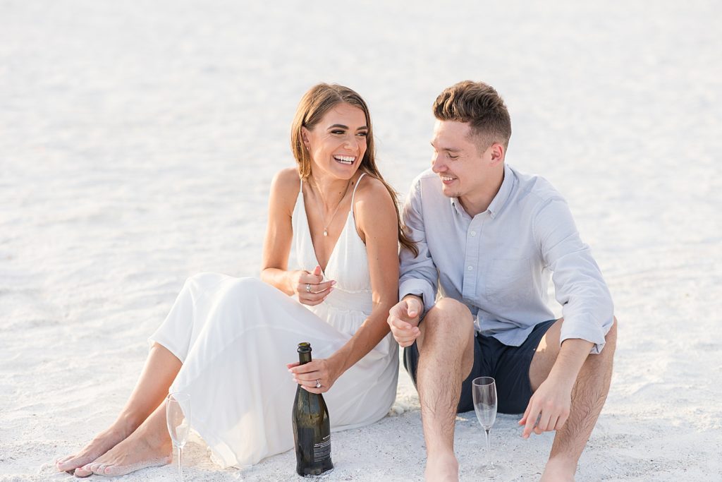 A couple having champagne on the beach during their Lido Key engagement session. 