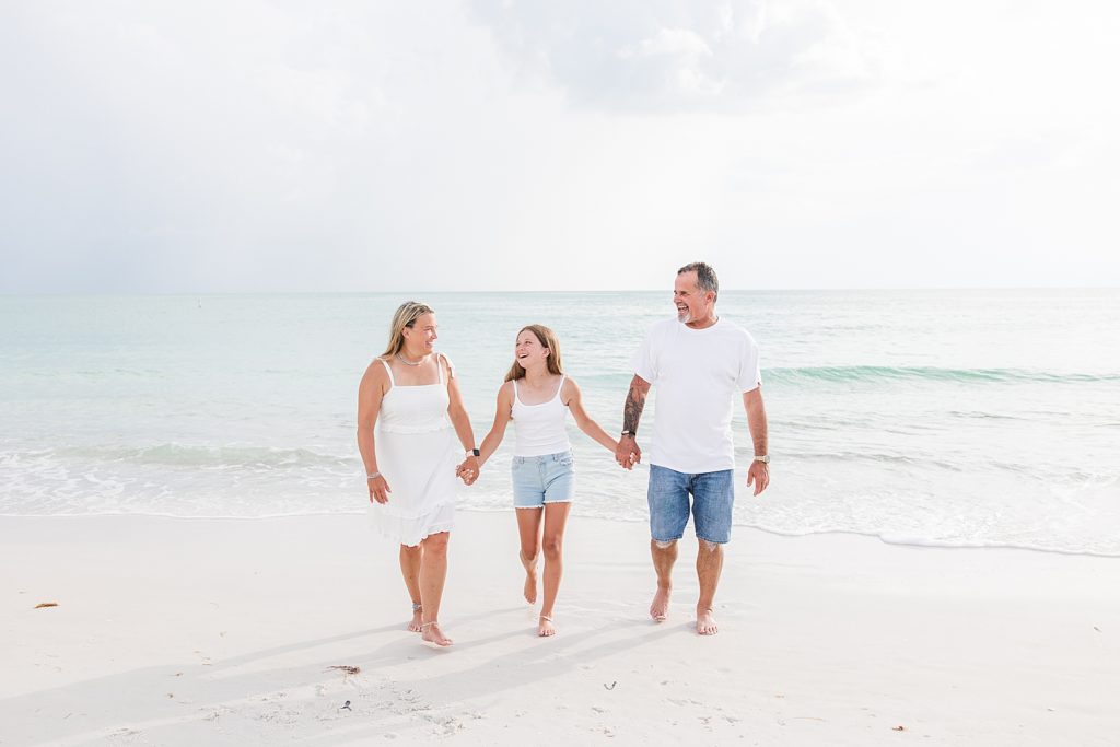 A family wearing white holding hands and walking down the beach. 