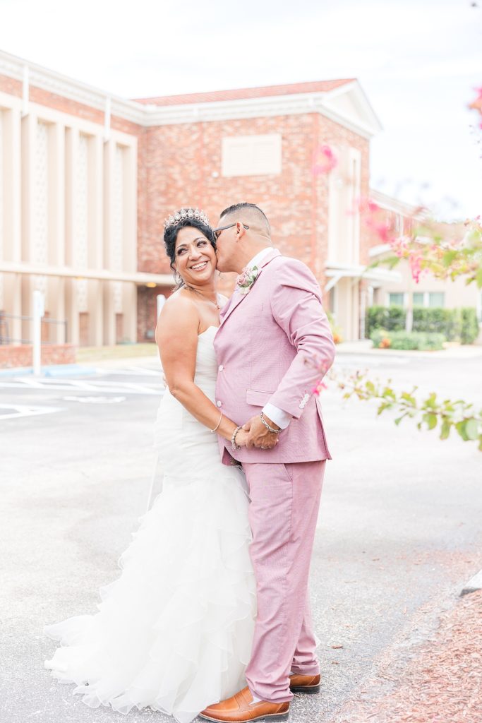 The groom wearing a blush pink suit kissing his bride. 