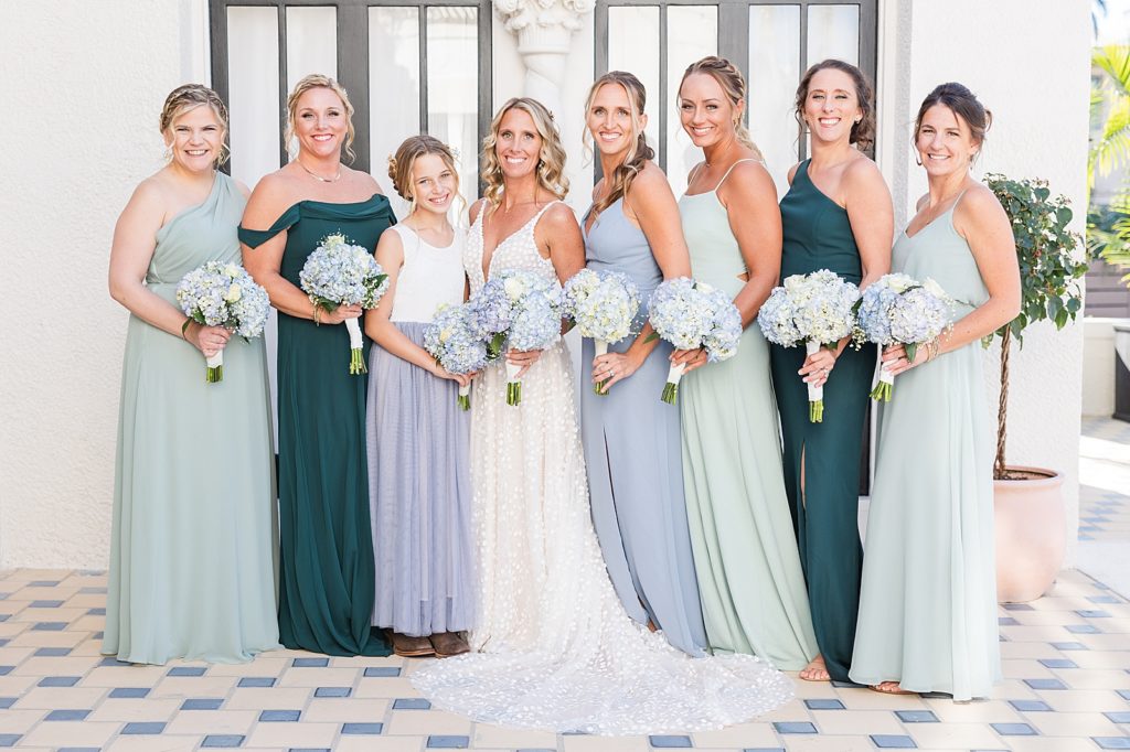 The bride and bridesmaids in different shades of blue and green dresses. 