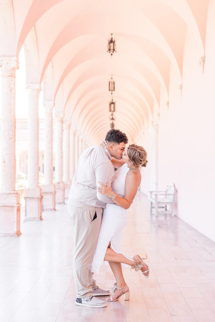Engaged couple kissing down the pink hallway of The Ringling Museum. 