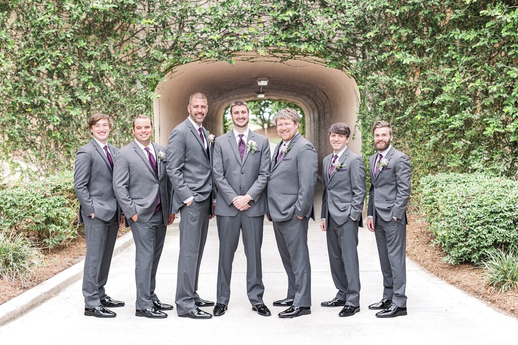 groom and groomsmen walking in front of an ivy tunnel.  