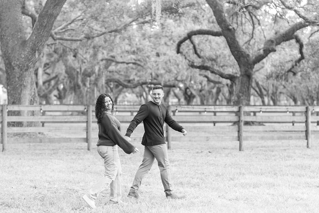 Black and white picture of an engaged couple walking through a field. 