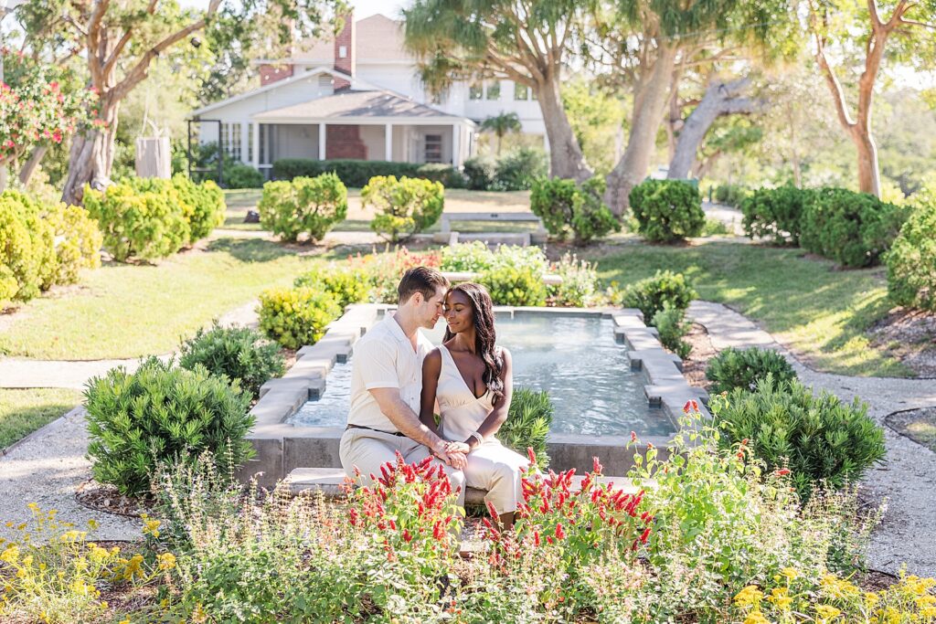 A engaged couple sitting on a bench in the middle of a garden. 