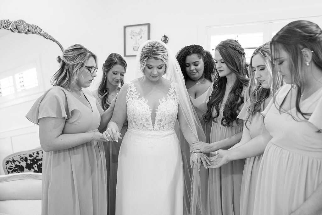 Black and white picture of the Bridesmaids praying over the Bride.