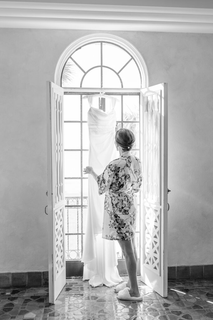 Bride looking at her dress hanging in the door. 