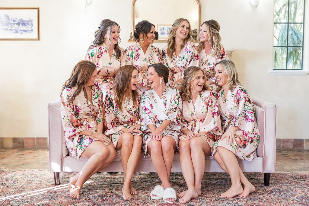 Bride and Bridesmaids laughing in a pink chair in their floral robes. 