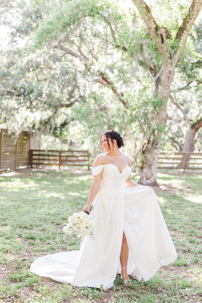 A picture of the bride wearing a white dress smiling at the oak trees. 