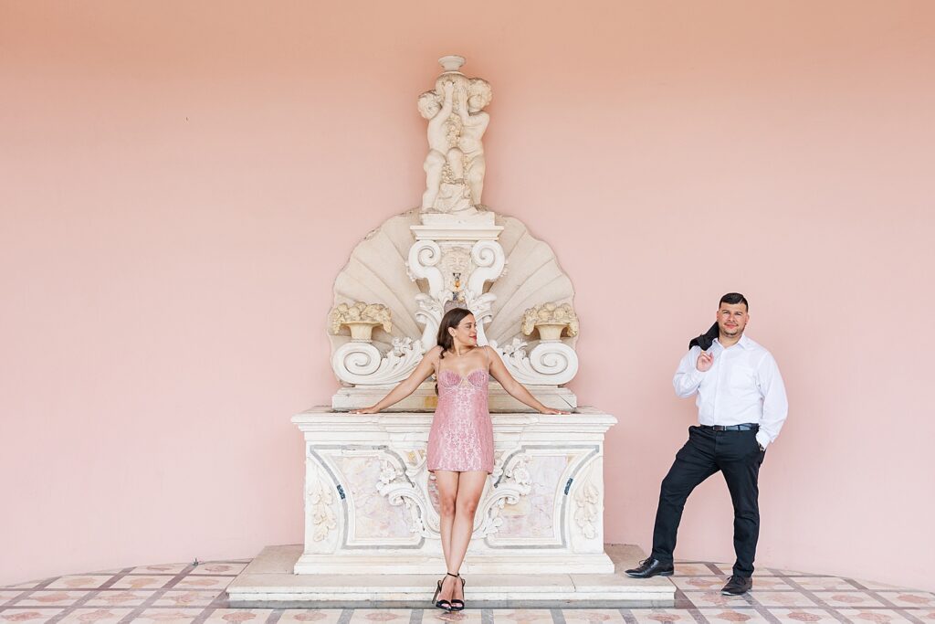 Woman wearing a pink dress looking at her Fiance' holding his black jacket over his shoulder.